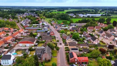 Tuğladan evler olan bir Hollanda köyünden geçen ana yol. Geleneksel tuğladan evler ve yeşil alanlar olan bir yerleşim alanı boyunca uzanan asfalt bir yolun havadan görünüşü.