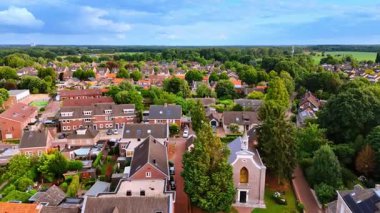 Köy çatıları ve beyaz çan kulesinin yüksek açılı manzarası. Çeşitli ev tasarımları, bahçeler ve yeşil bir banliyö bölgesindeki küçük beyaz çan kulesinin hava aracı görüntüsü..