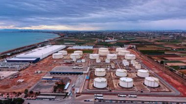 Alicante, Spain, 8 February 2026: Wide aerial shot of industrial terminal by the coast. Panoramic view of oil storage tanks near the sea under cloudy sky with distant city.