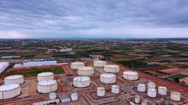 Alicante, Spain, 8 February 2026: Aerial view of oil storage facility and industrial zone. White fuel storage tanks at industrial site with agricultural fields and cloudy sky background.