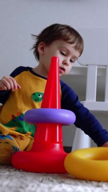 İki yaşında bir çocuk yerde oturuyordu. Küçük çocuk piramidi birleştirir ve ayağa kalkar. Dikey video
