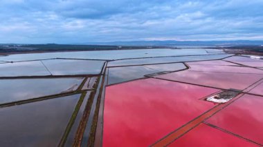 Kıyı manzarasında büyük pembe tuz buharlaşma göleti. Mavi sulara ve uzak dağlara karşı parlak pembe tuzlu su göletinin havadan bakış açısı.