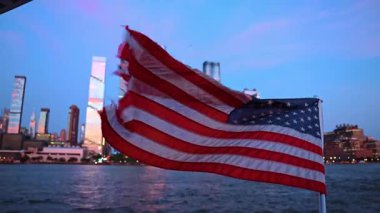American flag waves in the strong wind. Close up. Skyscrapers of Manhattan in the light f setting sun in the backdrop.
