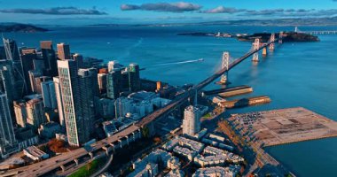 Gün batımında birçok araba Oakland Bay Köprüsü 'nden geçer. Şehir merkezindeki yüksek binaların üzerinden uçarak San Francisco, Kaliforniya, ABD 'deki körfez rıhtımına yaklaşıyor..