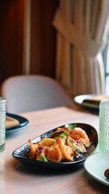 Dondurulmuş beyaz şarapla servis edilen deniz ürünleri tabağı. Siyah tabakta kaplanmış karides ve midye salatası ve beyaz şarap kadehi tutan bir kadın eli..