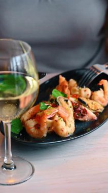 Close up of seafood plate with blurred white wine glass. Freshly prepared prawns and octopus salad with salmon roe served on black dish.