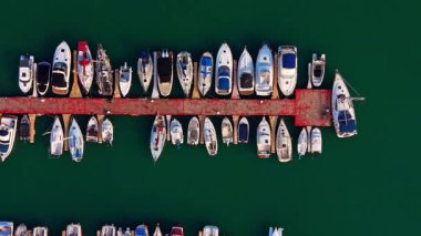 Rıhtıma yanaşmış yelkenlilerin yukarıdan görünüşü. Yeşil sudaki kırmızı rıhtıma demirlemiş yat ve yelkenlilerin detaylarını gösteren doğrudan tepe görüntüsü..