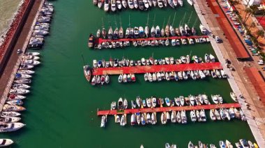Akdeniz limanındaki birçok yelkenli teknenin görüntüsü yükseldi. Sahil yolunun yakınındaki kırmızı rıhtımlara yanaşmış yelkenli ve sürat tekneleri ile dolu bir marinanın geniş hava görüntüsü..
