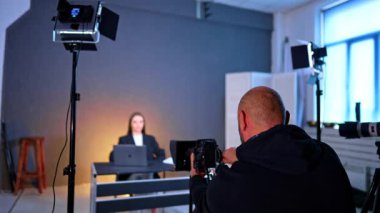 Modern stüdyoda çalışan bir kameramanın arka görüntüsü. Bulanık arka planda masada oturan kadını aydınlatır..