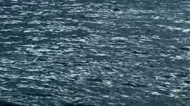 Karanlık dalgalı suyun soyut dokusu ve güneş ışığı. Çok sayıda küçük dalgalar ve parlak gümüş yansımalarla derin mavi su yüzeyinin yüksek açılı görüntüsü.