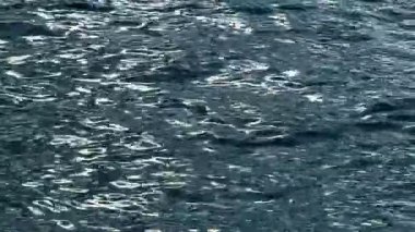 Parlak gümüş ışık yansımalı dalgalı karanlık deniz suyu. Küçük dalgalarla okyanus yüzeyinin detaylı görüntüsü ve mavi sudaki yüksek kontrastlı yansıtıcı gölgeler.