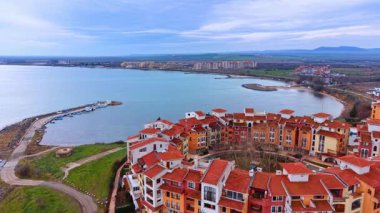 Deniz manzaralı tatil köyleri ve tekne iskelesi. Deniz kıyısında, bulutlu gökyüzünün altında küçük balıkçı tekneleri olan kırmızı çatılı evler..