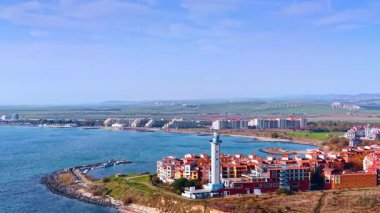 Deniz feneri ve mavi deniz manzaralı sahil kasabası. Kırmızı çatıları ve açık gökyüzünün altında mavi bir körfezin yanında beyaz bir deniz feneri olan modern kıyı mimarisi..