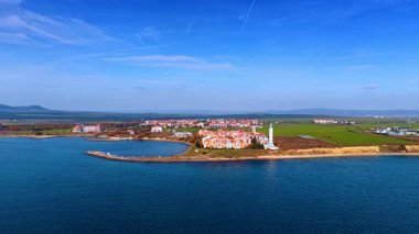 Denize yakın yarımadadaki kıyı kasabasının geniş hava manzarası. Mavi gökyüzünün altında su ve yeşil tarlalarla çevrili bir deniz kenarı yerleşiminin yüksek açılı görüntüsü.