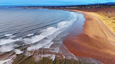 Dalgalı ve geniş kumlu kıyıları olan uzun bir kıyı şeridi. Paralel dalga hatlarının yüksek irtifa görüntüsü engin bir kumsala yaklaşıyor..
