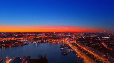 İsveç 'in Stockholm şehrinden nehrin yukarısına uçuş. Turuncu gökyüzü, gece şehrin ışıltılı manzarasının üzerinde..