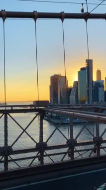 New York, ABD, 25 Eylül 2025: Günbatımında ünlü Brooklyn Köprüsü 'nde duruyor. Güneş batarken Manhattan 'ın görkemli gökdelenlerine bakın. Dikey video.