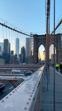 New York, ABD, 25 Eylül 2025: Gün batımında Brooklyn Köprüsü 'nden geçen arabaları izlemek. Arkaplanda Manhattan silueti var. Dikey video.