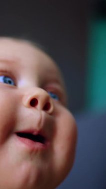 Beyaz, şirin, mavi gözlü bir bebeğin tombul yüzü. Kapatın. Kamera almaya çalışan meraklı bir çocuk. Dikey video