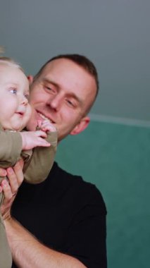 Babam küçük şirin bir bebeği elinde tutuyor. Anne çocuğu eğlendiriyor ve çocuk güzel güzel gülümsüyor. Düşük açı. Dikey video