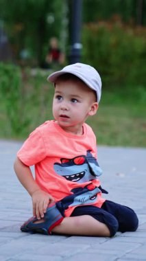 Küçük beyaz bir çocuk dışarıda, yerde oturuyordu. Çocuk ayağa kalkıp kameraya doğru koşuyor. Dikey video