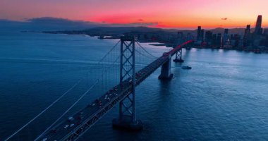 Oakland Bay Köprüsü 'nün desteğine kırmızı ışık yanarken yaklaşıyoruz. Gün batımında köprünün yanından bir sürü araba geçiyor. San Francisco, California, ABD.