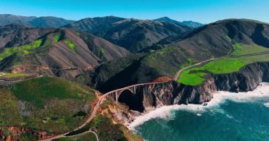 Kaliforniya Otoyolu 'ndaki Bixby Creek Köprüsü' nün havadan görüntüsü. Bixby Creek Köprüsü, kıyı dağları ve Kaliforniya Big Sur 'da Pasifik Okyanusu açık mavi gökyüzü altında.