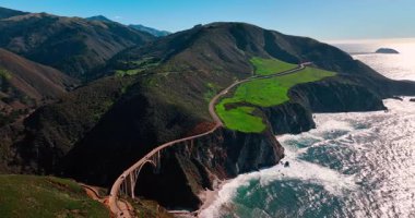 Otoyol 1, Bixby Köprüsü 'ne doğru yeşil tepeleri geçiyor. Yeşil dağ manzaralarıyla çevrili kıyı otoyolu ve köprünün hava perspektifi.