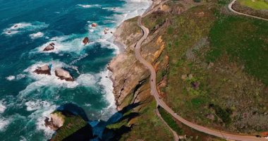 Pasifik Okyanusu 'nun yukarısındaki engebeli uçurumlardaki sahil yolu. Kaliforniya 'da dalgaların kayalara çarptığı sarp kayalıklar boyunca 1. Otoyol kıvrımlı.