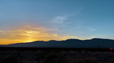 Canlı turuncu çöl günbatımında sıradağların silueti. Dağların silueti ve çöl bitkisi parlak turuncu ve mavi günbatımı gökyüzüne karşı ince bulutlarla.