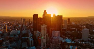 Parlak güneş, Los Angeles, Kaliforniya, ABD şehir merkezindeki gökdelenler grubunun arkasından parlıyor. İnsansız hava aracı görüntüleri şehir merkezine iniyor..