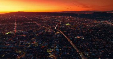 Los Angeles, California, ABD manzarası boyunca yoğun karayolu boyunca uçuş. Gün batımında turuncu gökyüzüne bakan sokak lambalarıyla şehrin manzarası..