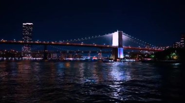 Gece vakti karanlık nehir manzaralı Brooklyn Köprüsü 'ne yaklaşıyoruz. Tekneden New York 'un simgeleri.