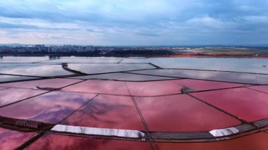 Geniş pembe göllerle çevrili tuz yığınlarına yaklaşıyoruz. Bulutlar tuz üretimi için hayati önem taşıyan doğal kaynakların pembe sularını yansıtıyor.