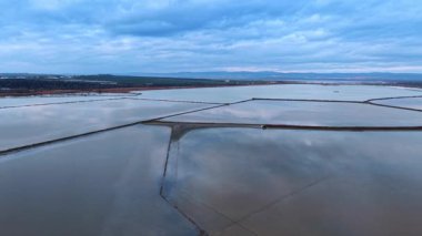 Vast pans with peaceful water reflecting cloudy sky. Salty ponds for salt crystallization for industrial production.