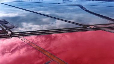 Flight above the salterns reflecting cloudy sky. Special ponds with pink water used for salt production.