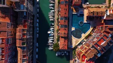 Yüzme havuzlu bir apartman. Dikey İHA perspektifi çatıları, mavi bir havuzu ve dar bir liman kanalına yanaşmış tekneleri gösteriyor..