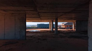 One of the floors of the multi-storied building with some bulkheads and columns. Rubbish and puddles are on the floor.