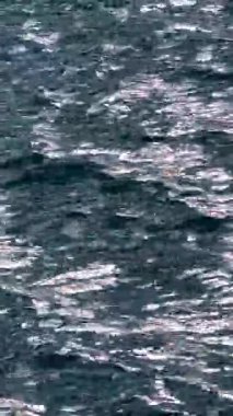 Parlak güneş yansımalarıyla dalgalanan koyu mavi okyanus suyu. Koyu deniz suyu yüzeyinin yüksek kontrastlı dokusu ve dağınık beyaz güneş ışığı gölgeleri..