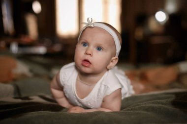 Sarı elbiseli bir bebek ve yatak odasındaki yeşil battaniyenin üzerinde karnında bir bandaj var.