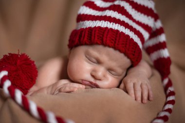 Yeni doğmuş bir bebek kırmızı çizgili bir şapkayla bej bir battaniyenin üzerinde yatıyor.