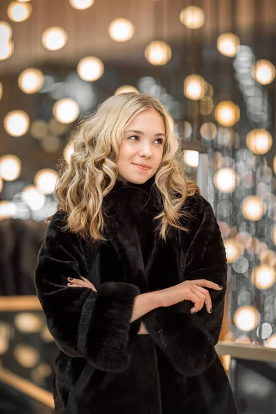 A girl in a black fur coat among the lights of the shopping center