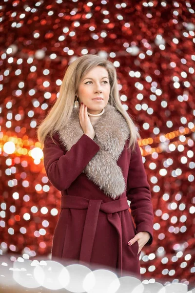 A girl in a red fur coat among the lights of the shopping center
