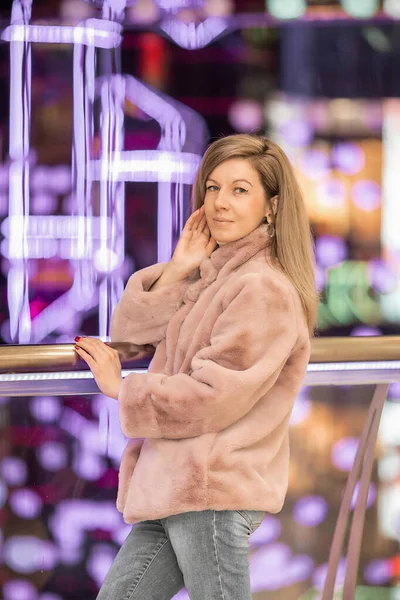 A girl in a beige fur coat among the lights of the shopping center