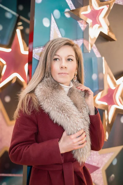 A girl in a red fur coat among the lights of the shopping center