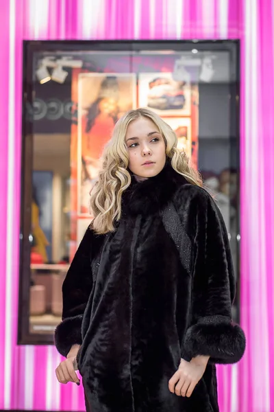A girl in a black fur coat among the lights of the shopping center