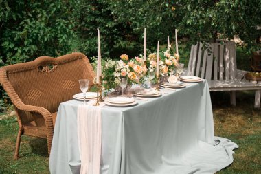 Mumlar, bardaklar ve çiçeklerle süslenmiş şenlikli bir düğün masası. Dekor turuncu ve yeşil tonlarda yapılır. Kapatın. Tabaklarda davetli listesi ve dilekleri var..