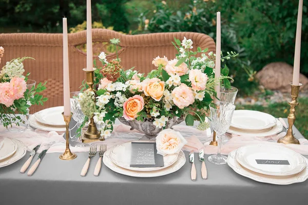 A festive wedding table with candles, glasses, decorated with flowers. The decor is made in orange and green tones. Close up. On the plates are guest lists and wishes.