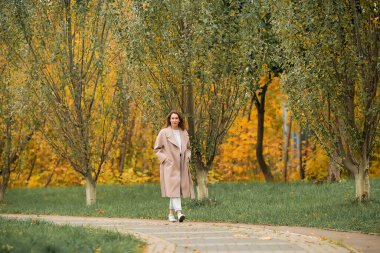 Pembe ceketli ve kot pantolonlu beyaz bir kız sonbahar parkında dans ediyor.