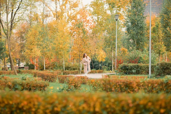 Biała Dziewczyna Różowym Płaszczu Niebieskich Dżinsach Otworami Tańczy Jesiennym Parku — Zdjęcie stockowe
